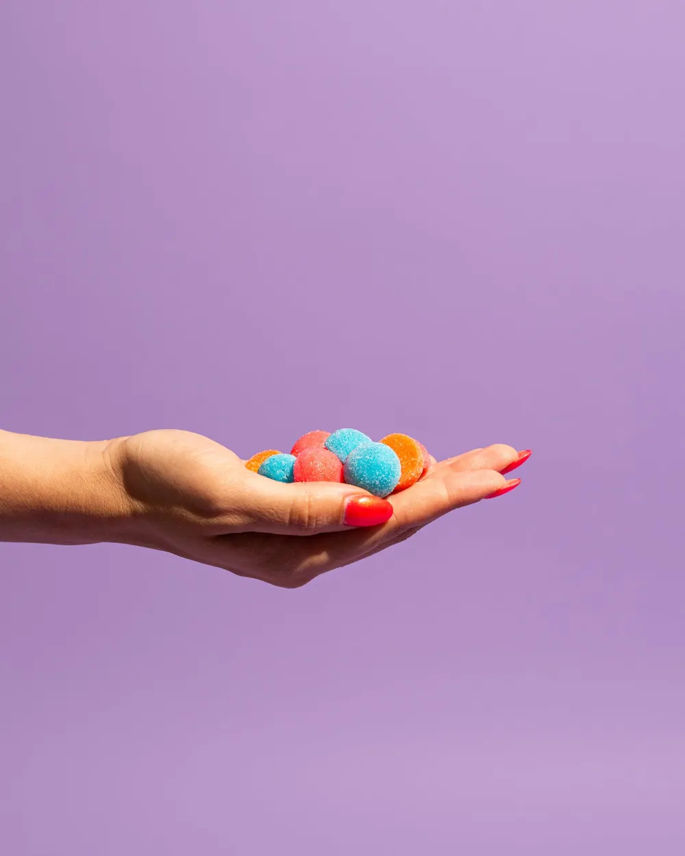 A hand holding a pile of sugar-coated Gummy Gainz gummies against a purple background